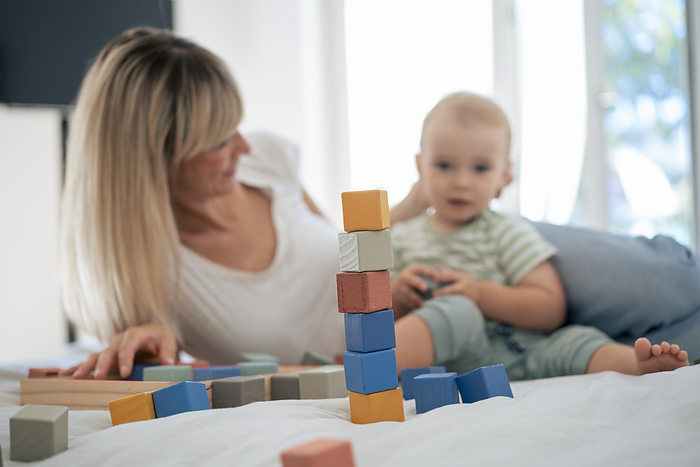 Stack of toy blocks with mother and son on bed at home