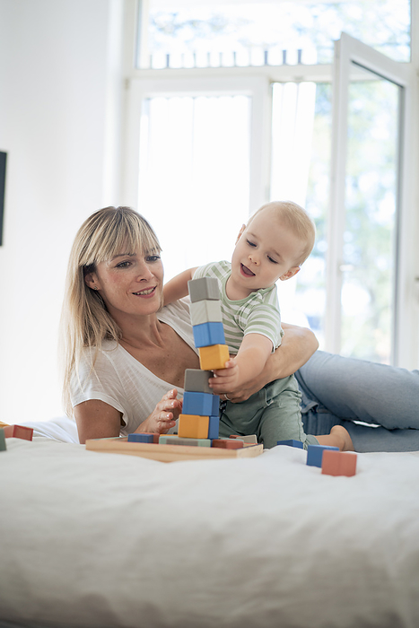 Mother and son playing with toy blocks game on bed at home