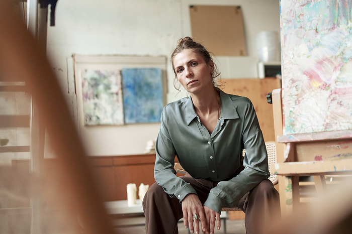 Confident painter sitting on chair in art studio