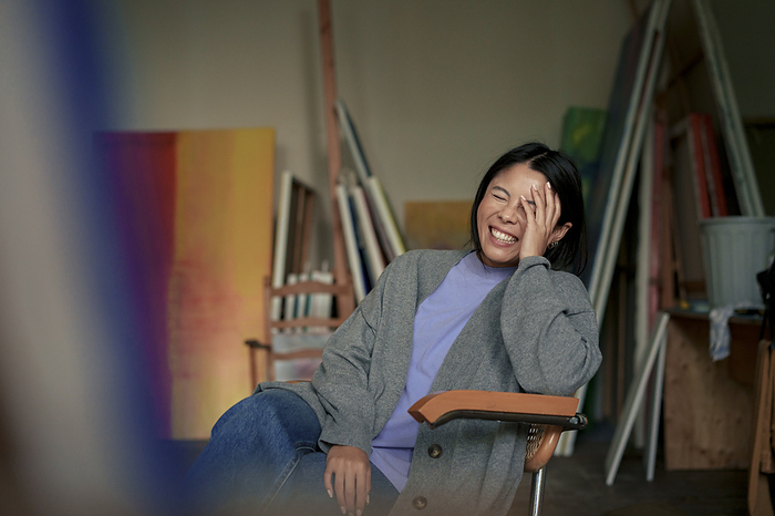 Happy painter with eyes closed sitting on chair in art studio