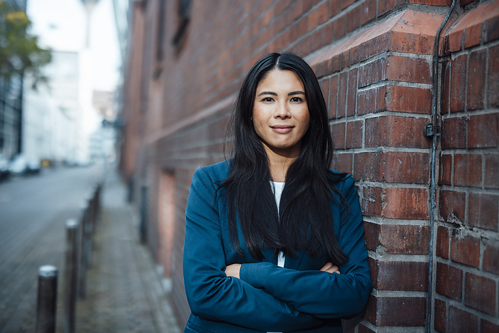 Smiling businesswoman standing with arms crossed near brick wall
