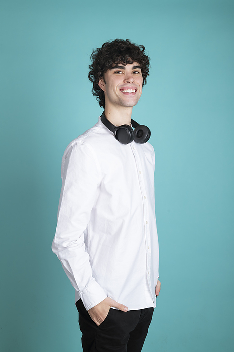 Smiling man with wireless headphones standing against cyan background