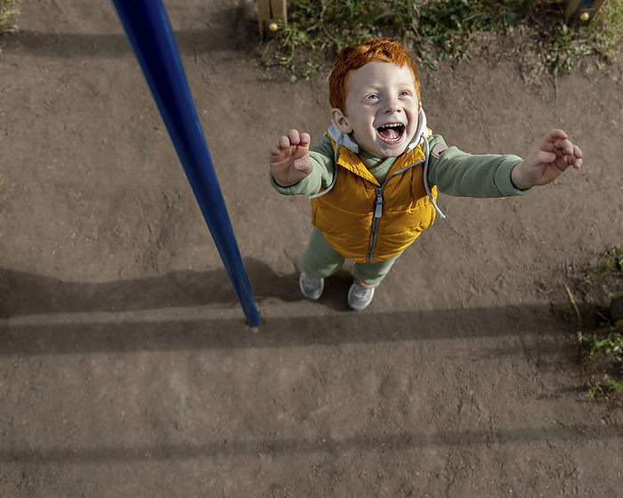 Happy redhead boy standing with arms raised at playground