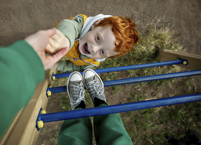 Playful boy holding mother's hand on ladder at playground