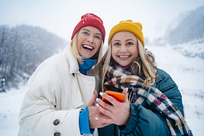 Smiling friends standing with smart phone on snowcapped mountain