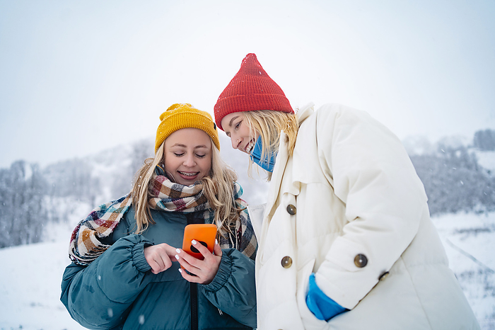 Smiling woman using and showing smart phone to friend on snowcapped mountain