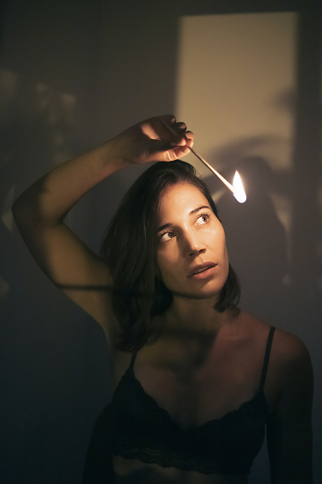 Young woman portrait with matches Woman holding ignited matchstick in front of wall