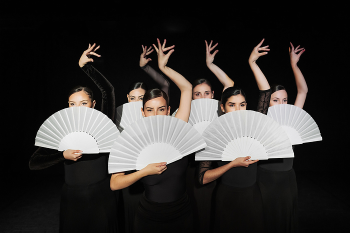 Madrid, Spain. Spanish dance and flamenco students practising with their dance teachers.  Group of flamenco dancers holding hand fans and dancing against black background