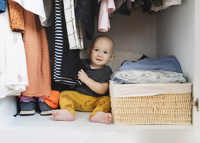 Cute boy playing with clothes in closet at home