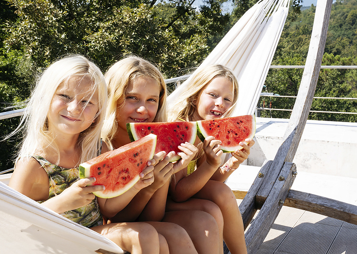 Smiling sisters sitting on hammock with slices of watermelons