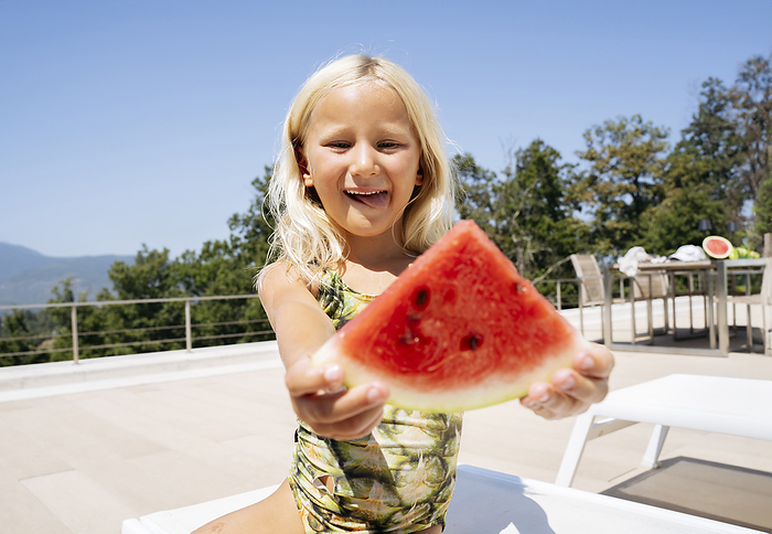 Smiling girl sitting and holding slice of watermelon on lounge chair