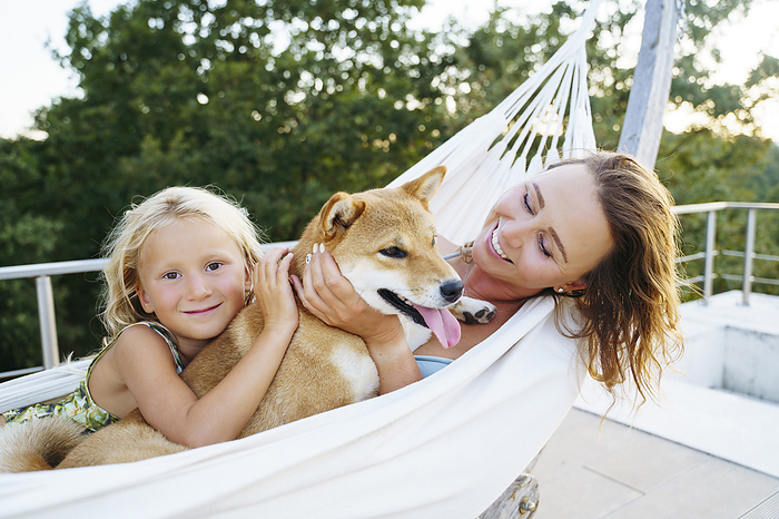 Smiling mother and daughter petting Shiba Inu dog in hammock