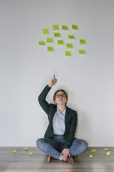 Businesswoman sitting on ground and pointing at adhesive notes