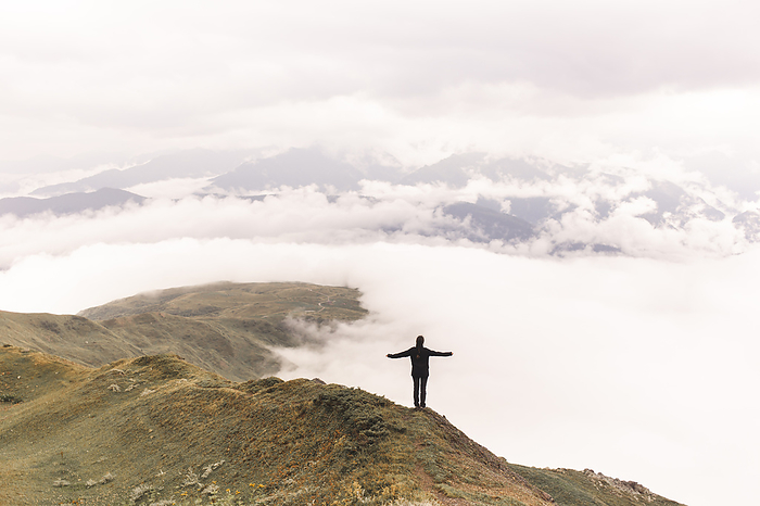 Woman with arms outstretched standing on Mestia mountain near clouds