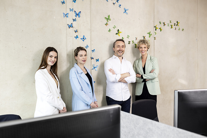 Smiling colleagues standing in front of wall with butterflies stickers at office