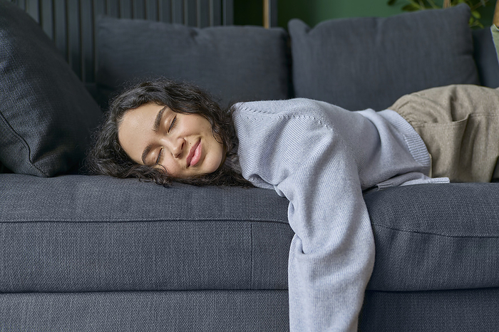 Smiling woman lying down on sofa with eyes closed at home