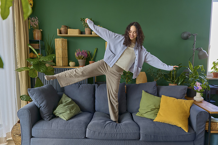 Playful woman balancing on sofa at home