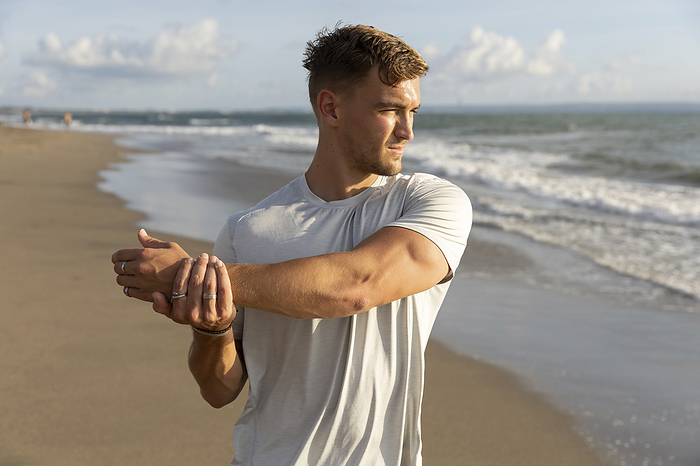 Young man stretching arm at beach
