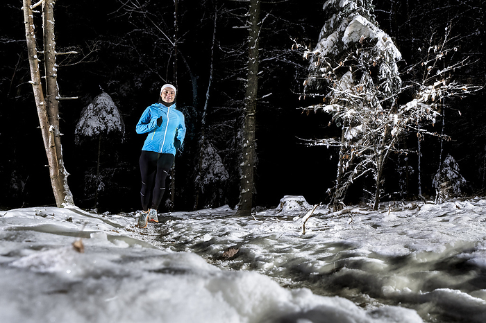 Young woman running in winter forest at night