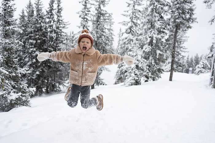Happy girl jumping on snow in winter forest