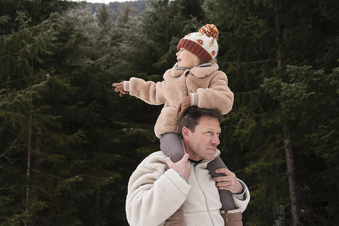 Father carrying daughter on shoulders near trees in winter forest
