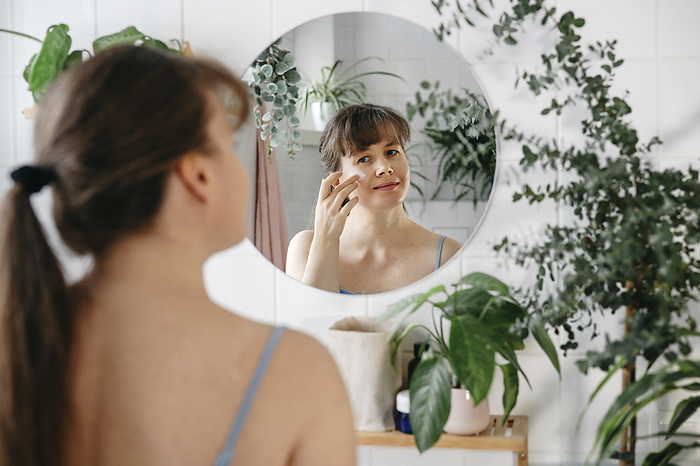 Woman applying cream on face in front of mirror