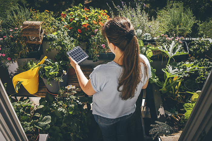 Woman holding solar battery near plants in balcony