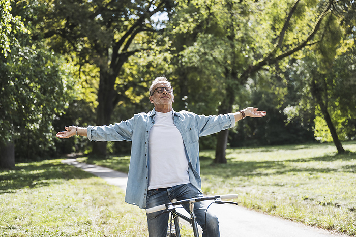 Carefree senior man with arms outstretched sitting on bicycle in park