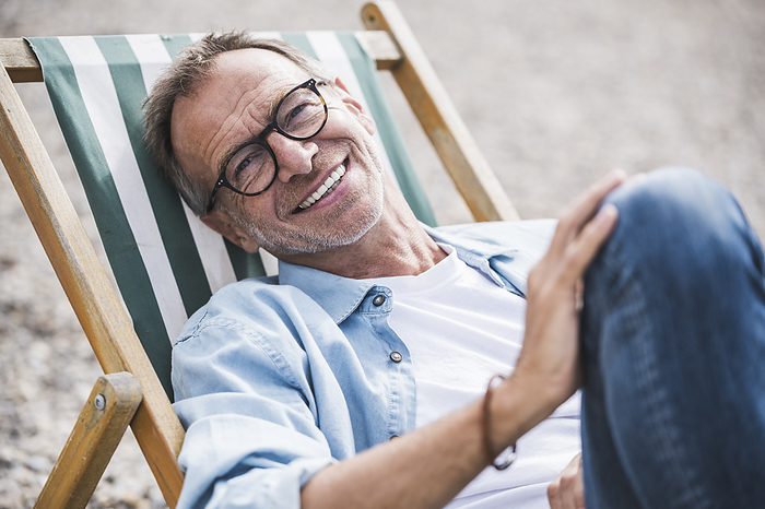 Happy senior man sitting on deck chair at beach