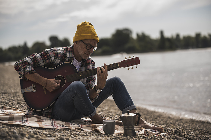 Senior man playing guitar sitting by sea on weekend