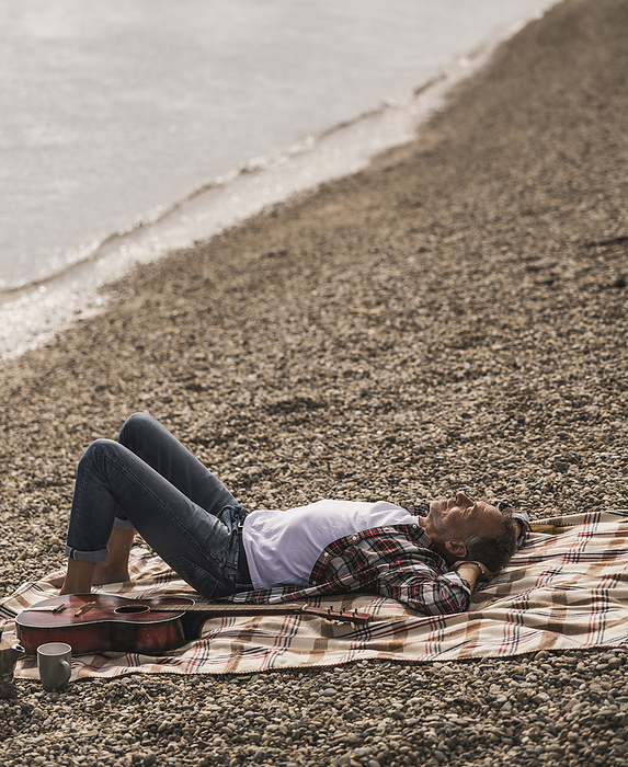 Senior man resting on blanket by sea at beach