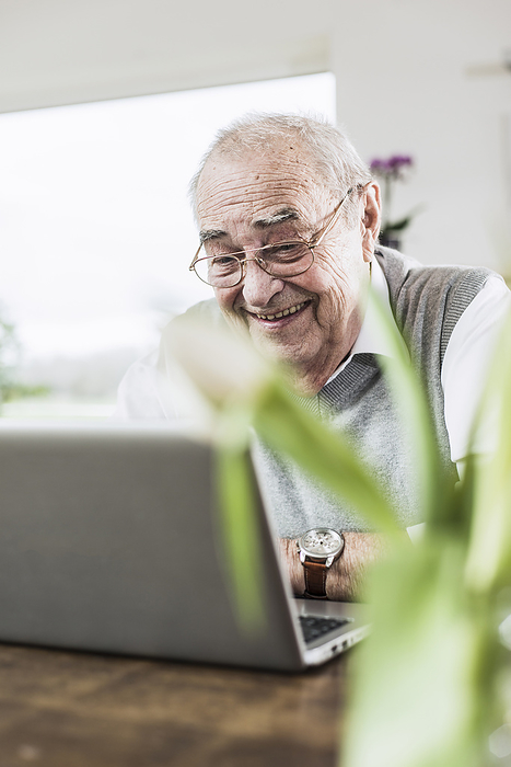 Smiling senior man talking on video call through laptop at home