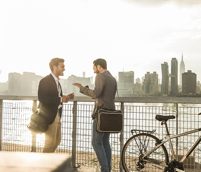 Happy colleagues talking by river at sunset in New York City, USA