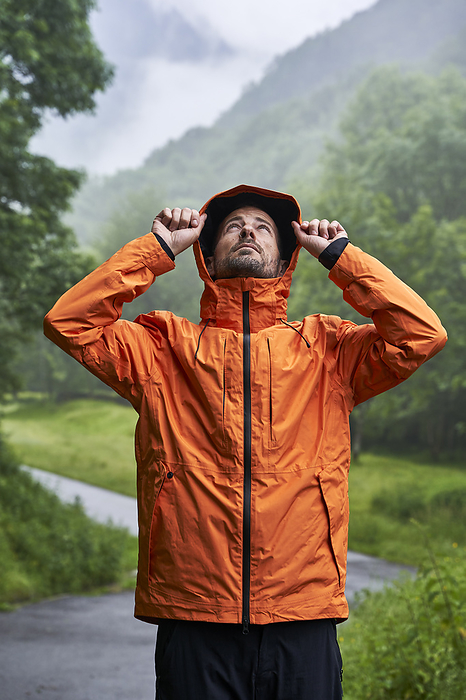 Man wearing orange jacket and standing in front of Pyrenees mountain on road