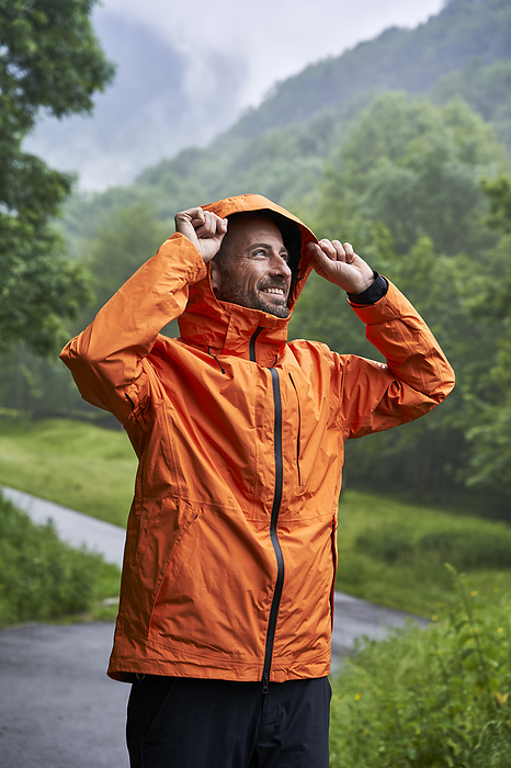 Happy man wearing orange jacket and standing in front of mountain