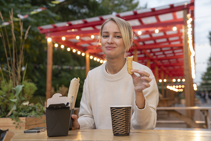 Smiling blond woman eating food at table in amusement Park
