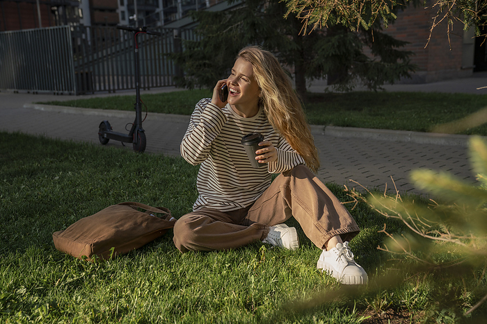 Blond woman talking over smart phone sitting on grass