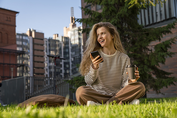 Happy woman with mobile phone sitting on grass in park