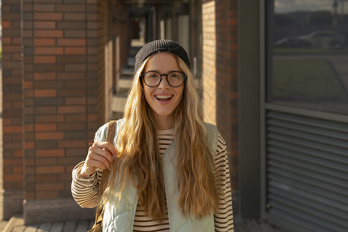 Happy blond woman wearing eyeglasses and knit hat on footpath