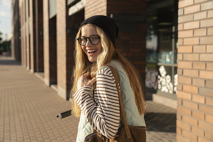 Smiling woman with shoulder bag standing on footpath