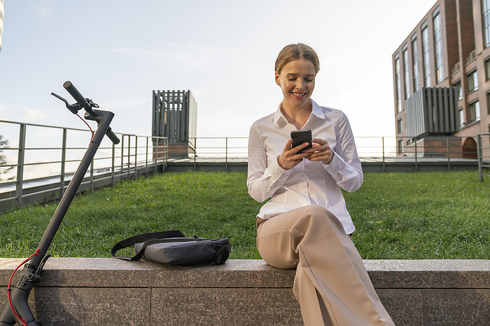 Businesswoman text messaging over smart phone sitting on wall