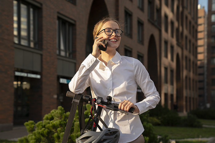 Smiling businesswoman with electric push scooter talking on smart phone