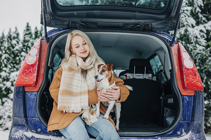 Smiling woman sitting in car trunk with pet dog