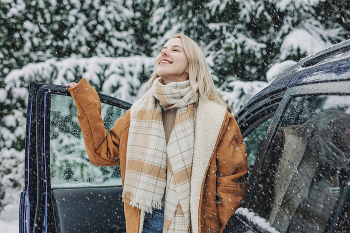 Smiling woman standing by car door on snowy day