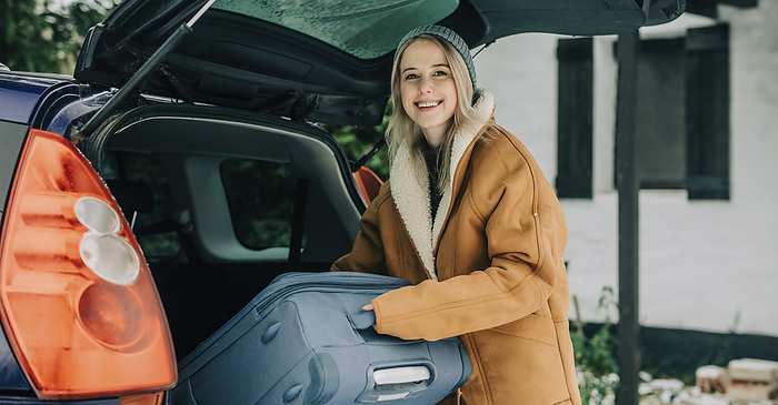Happy woman putting suitcase in car trunk