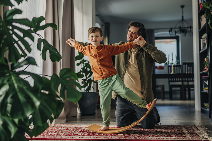Smiling father helping son to balance on board at home