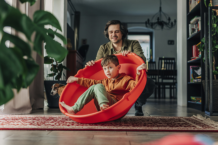 Smiling father spinning son on plastic container at home