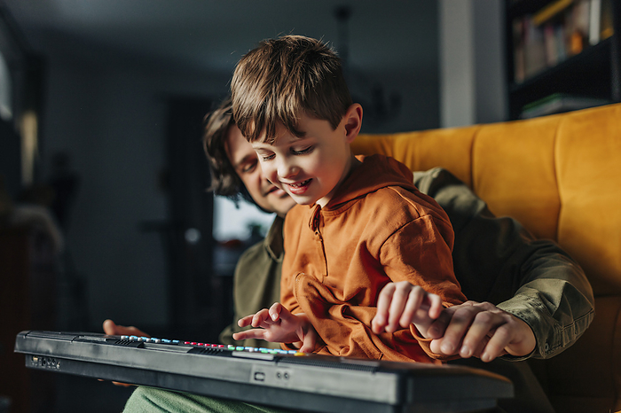 Smiling father teaching son to play electric piano at home