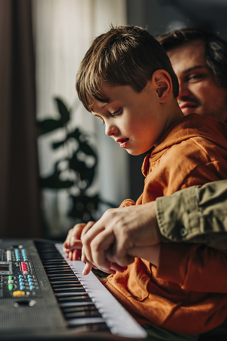 Father holding hands and teaching electric piano to son at home