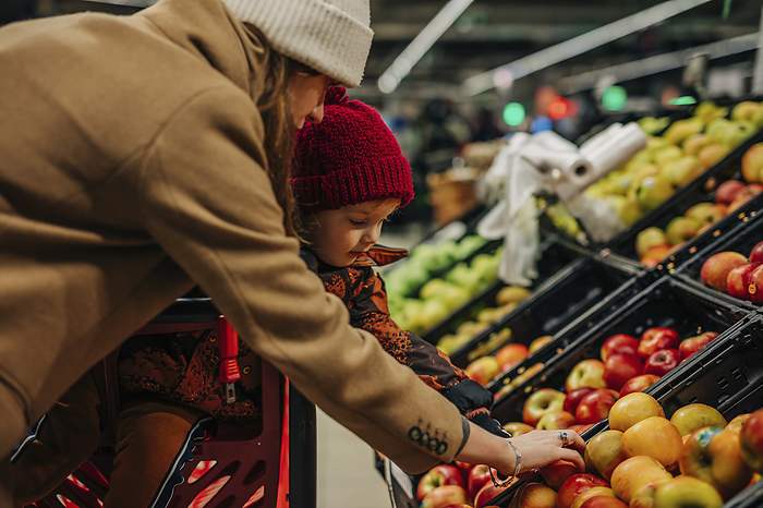Young woman and son buying apples at supermarket